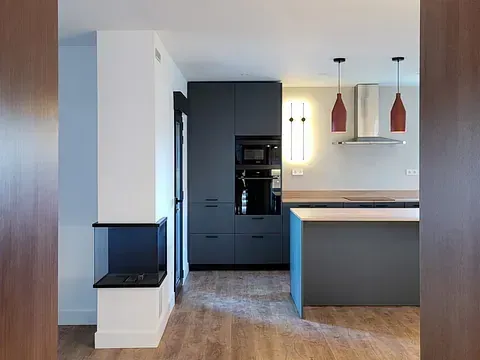 Cocina moderna con gabinetes grises, pisos de madera y luces colgantes rojas.