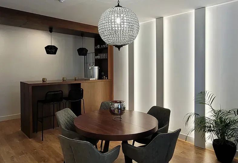 Un comedor con mesa redonda, sillas y barra. Una lámpara de araña de cristal cuelga sobre la mesa.