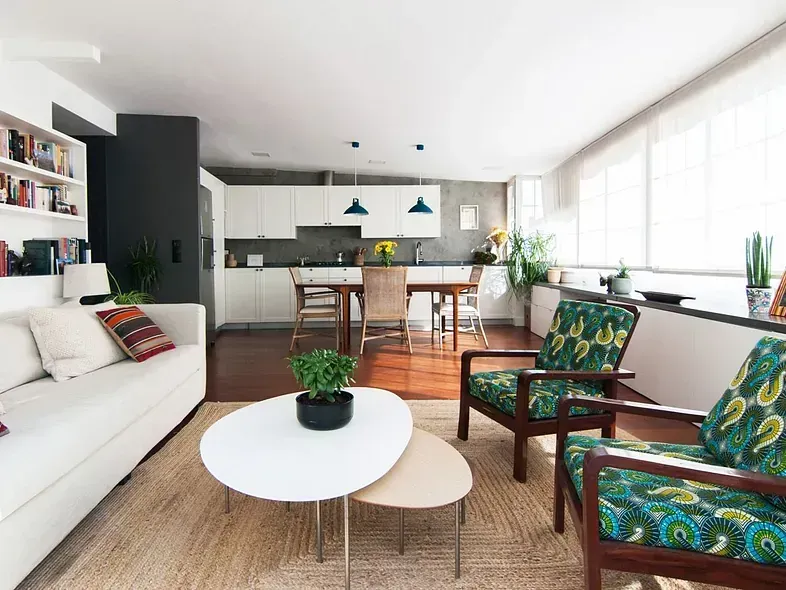 Sala de estar con sofá blanco, sillones estampados y cocina abierta.