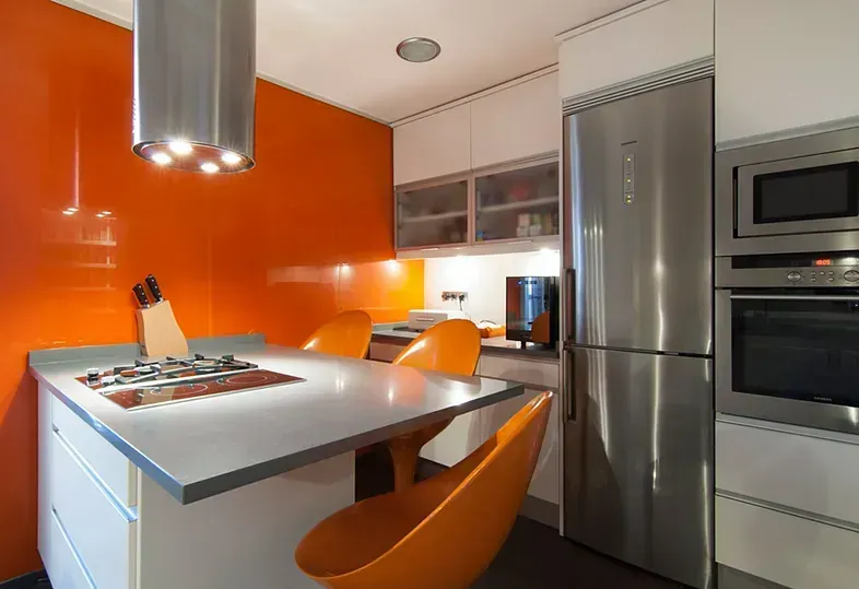 Cocina moderna con detalles en naranja, electrodomésticos de acero inoxidable y encimera gris.