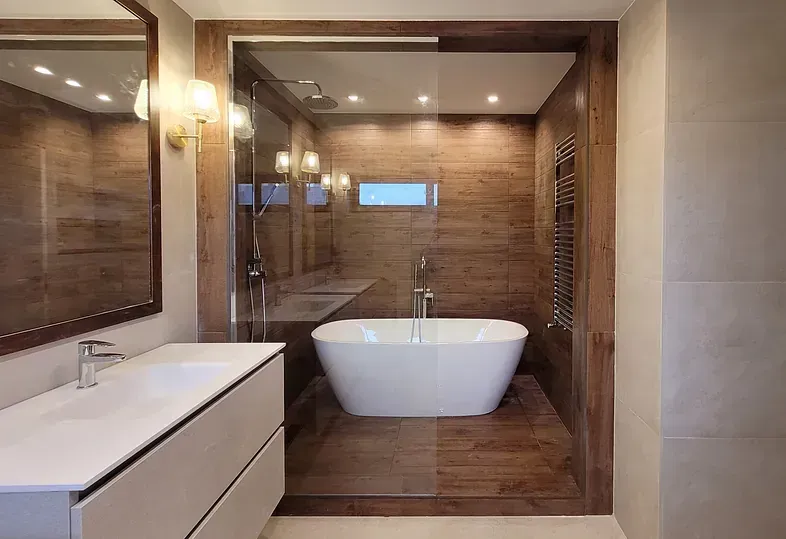 Baño moderno con bañera blanca, paneles de madera, ducha de cristal y tocador.