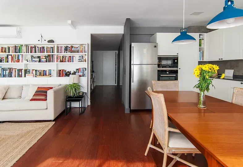 Sala de estar con comedor. Estanterías, sofá blanco, suelos de madera y cocina con electrodomésticos de acero inoxidable.