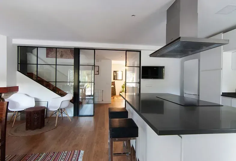 Cocina moderna con isla con encimera negra y pared de cristal hasta las escaleras.