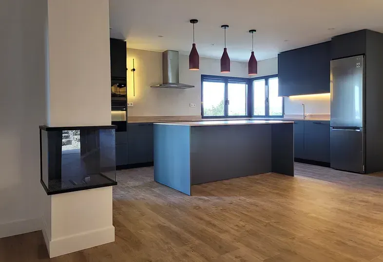 Cocina moderna con gabinetes grises, pisos de madera y chimenea blanca.