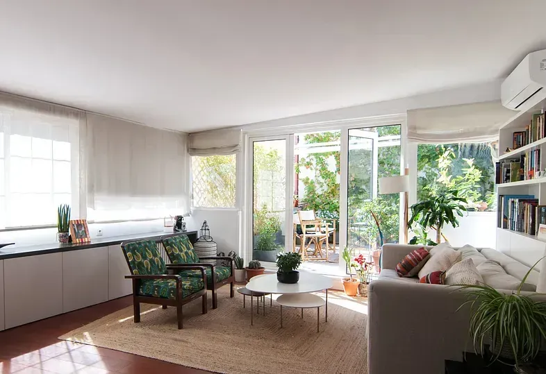 Luminoso salón con puertas abiertas a un balcón. Dos sillones estampados y un sofá dan al balcón.