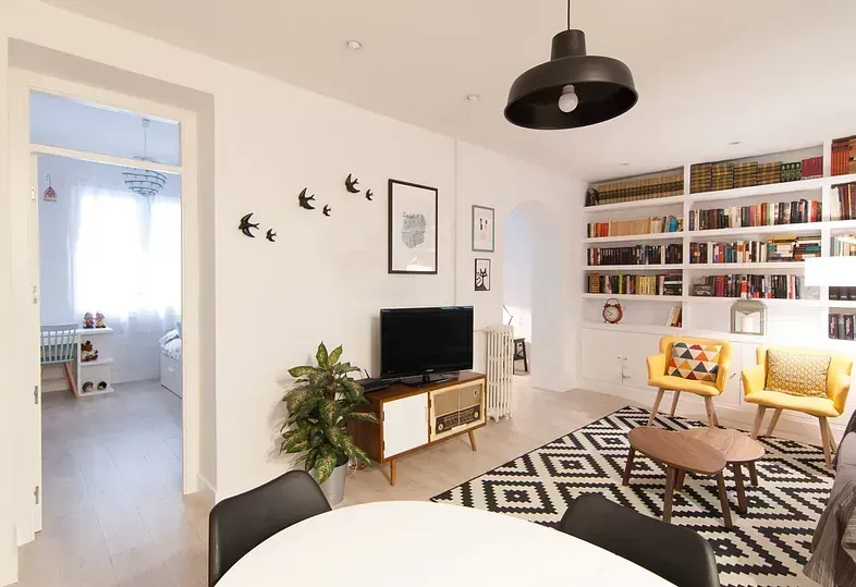 Sala de estar con estanterías empotradas, televisor y dos sillas amarillas. Una mesa redonda en primer plano.