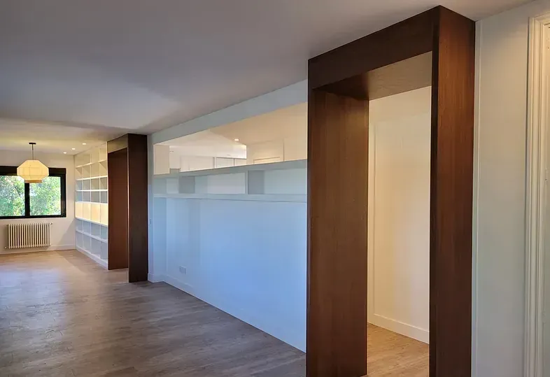 Habitación vacía con arcos y estantes de madera, pisos de madera clara y paredes blancas.