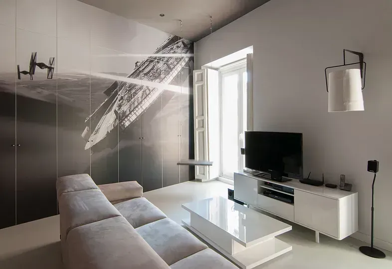 Sala de estar moderna con sofá blanco, TV y mural abstracto.