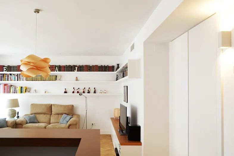 Sala de estar con paredes blancas, estanterías empotradas, sofá beige y lámpara de madera.