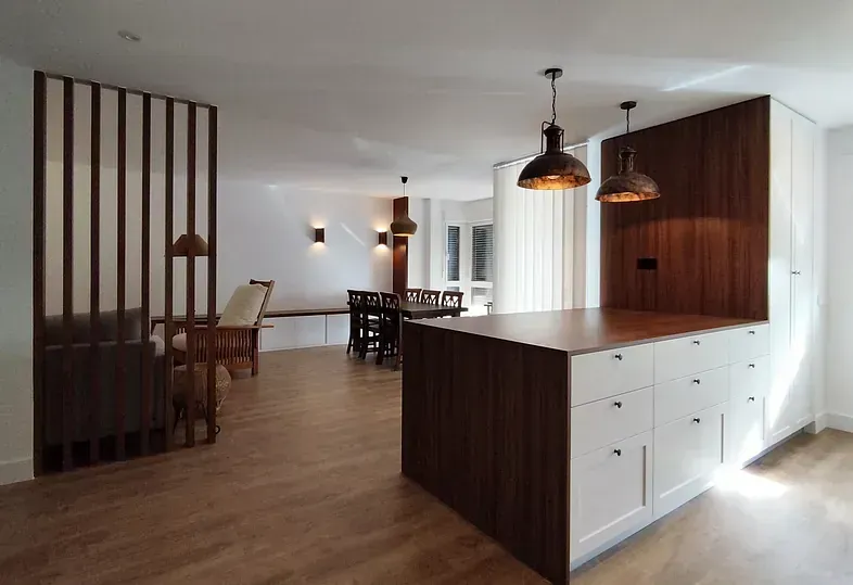 Cocina moderna de concepto abierto con isla de madera y color blanco, biombo de listones de madera y zona de comedor.