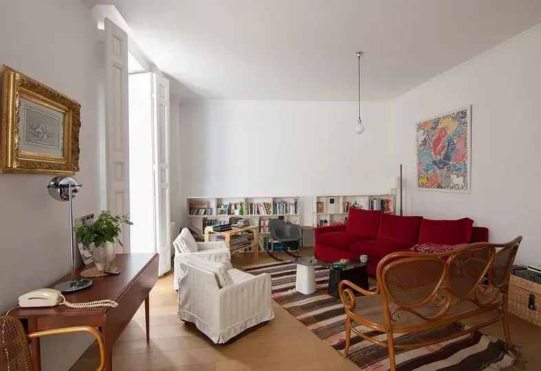 Sala de estar con un sofá rojo, sillas blancas y una estantería larga.