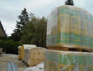 Des matériaux de construction emballés, empilés à l'extérieur sur des palettes, à côté d'arbres et d'une allée.