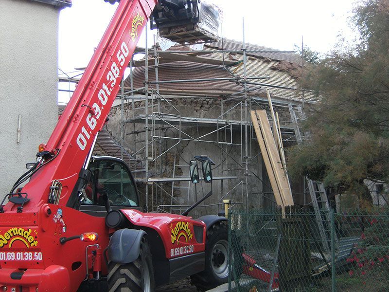 Camion-grue rouge à côté d'une maison en construction avec des échafaudages et une échelle.