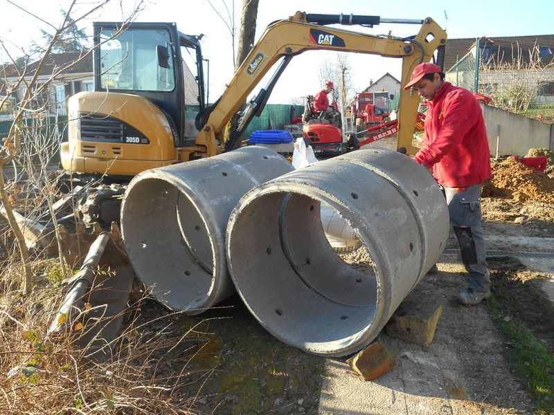 Des ouvriers du bâtiment se trouvent à côté d'une excavatrice et de gros tuyaux en béton sur un chantier en bord de route.