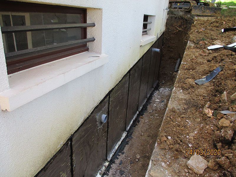 Mur extérieur du sous-sol avec étanchéité noire et une tranchée de drainage étroite à côté d'une fenêtre de maison