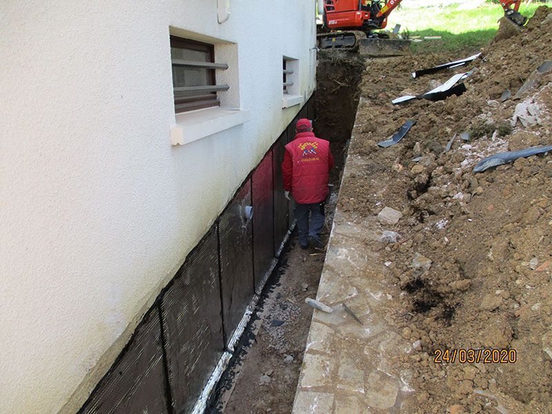 Ouvrier en veste rouge dans une tranchée étroite à côté des fondations d'une maison en construction.