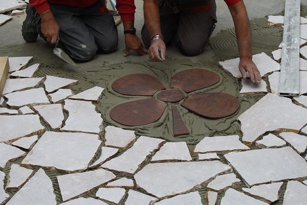 Des ouvriers installent une mosaïque à cinq pétales sur une terrasse en pierre