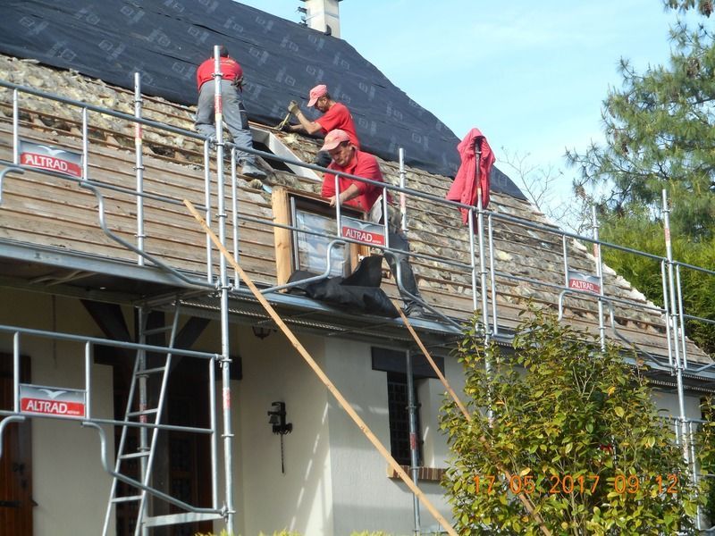 Des ouvriers en tenue rouge réparent un toit sur un échafaudage à côté d'une maison