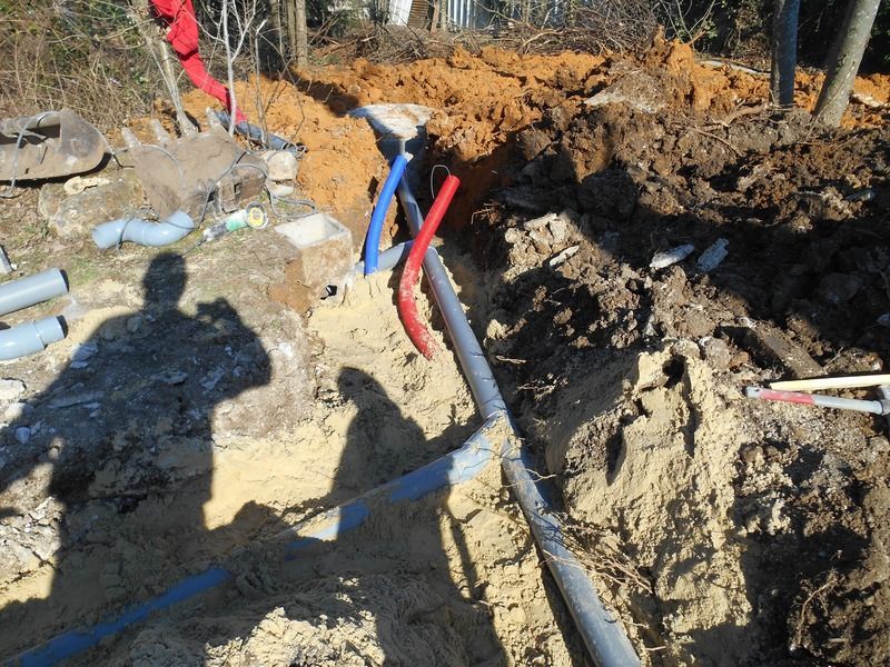 Chemin de terre creusé avec tuyaux apparents et conduits rouges, bleus et noirs sur un chantier de construction