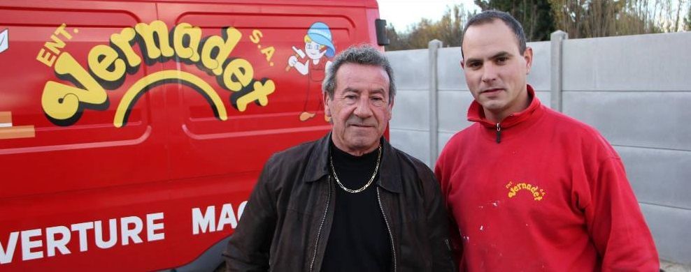 Deux hommes se tiennent devant une camionnette de livraison rouge avec des inscriptions jaunes.