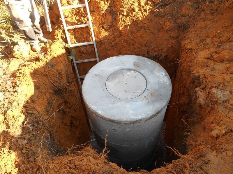 Fosse d'excavation avec une grande cuve cylindrique grise et une échelle adossée à la paroi de terre