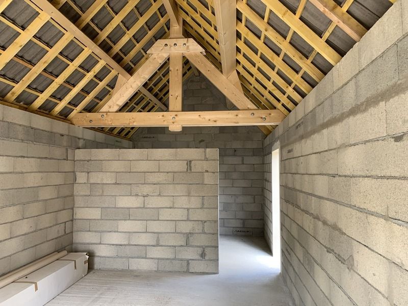 Pièce en parpaings inachevée avec charpente apparente et une petite ouverture de fenêtre.