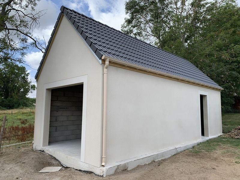 Petit cabanon blanc avec toit à pignon gris et porte ouverte de style garage dans une cour rurale