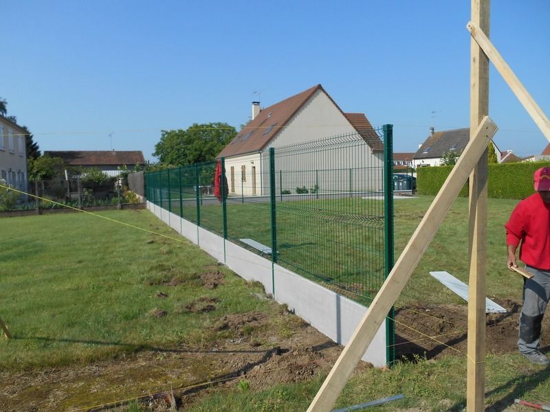 Une nouvelle clôture verte borde une cour gazonnée et des maisons par une journée ensoleillée.