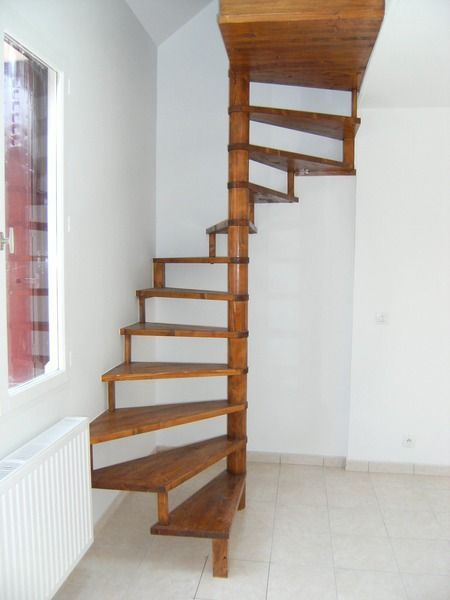 Escalier en colimaçon en bois dans une pièce blanche et lumineuse, à côté d'une fenêtre et d'un radiateur