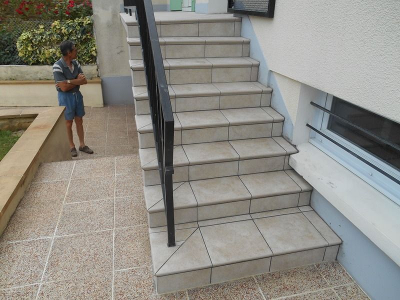Une personne se tient à côté d'un escalier extérieur avec des rampes noires et des marches carrelées.