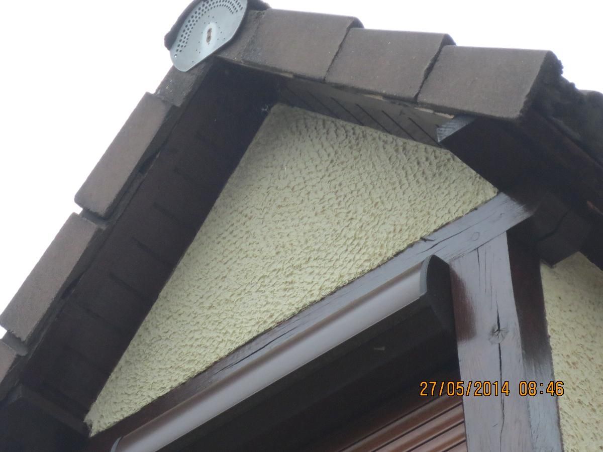 Gros plan sur le pignon d'un toit de maison, avec des bardeaux foncés et un panneau mural texturé clair.
