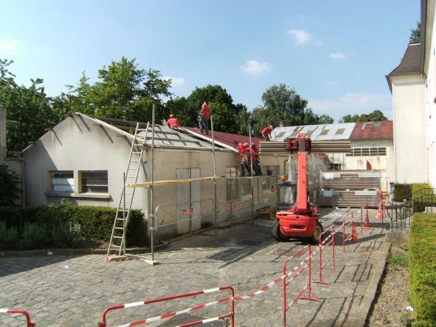Chantier de construction avec une maison en réparation, des échafaudages et une nacelle élévatrice rouge.