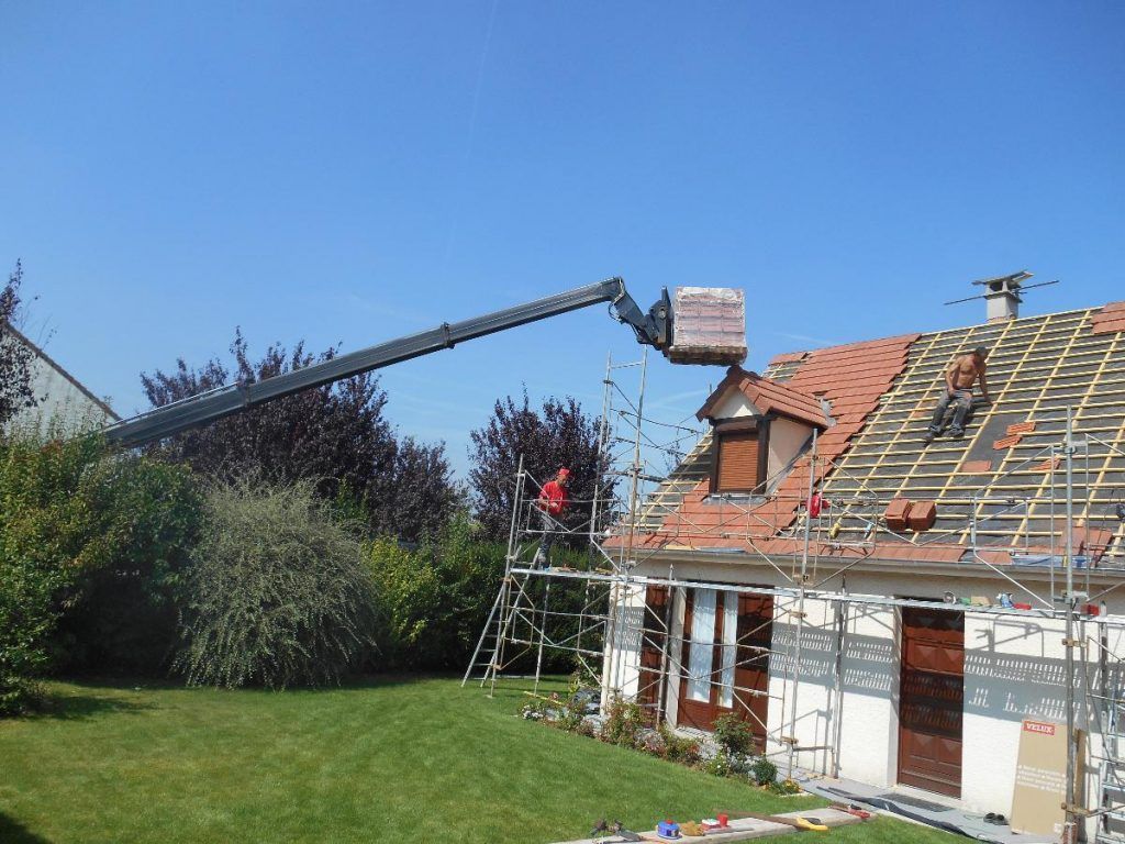 Réparation du toit d'une maison à l'aide d'échafaudages et d'une nacelle élévatrice sous un ciel bleu dégagé.
