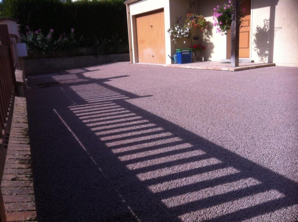 Allée ensoleillée aux longues ombres rayées menant à un garage et à des fleurs en pot près du mur