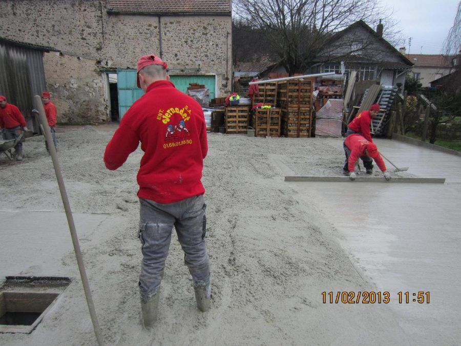 Des ouvriers en vestes rouges lissent le béton frais sur un chantier de construction en extérieur