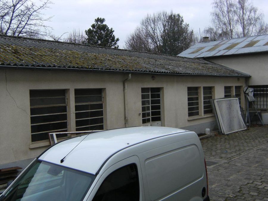 Une camionnette blanche garée dans une cour pavée à côté d'un bâtiment beige aux nombreuses fenêtres