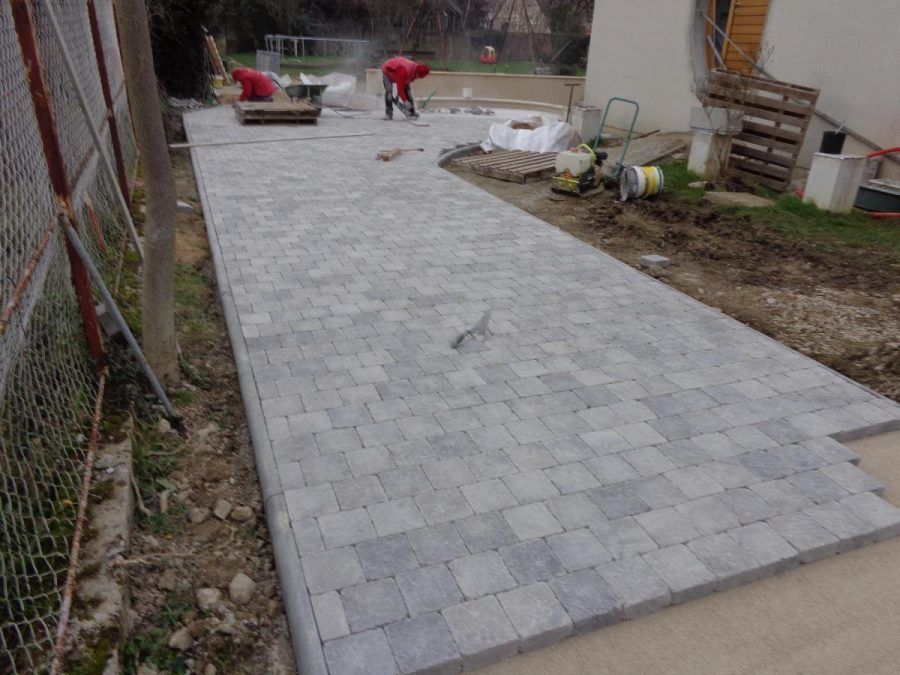 Allée en pavés de pierre en construction à côté d'une maison, avec des ouvriers et des outils dans la cour.