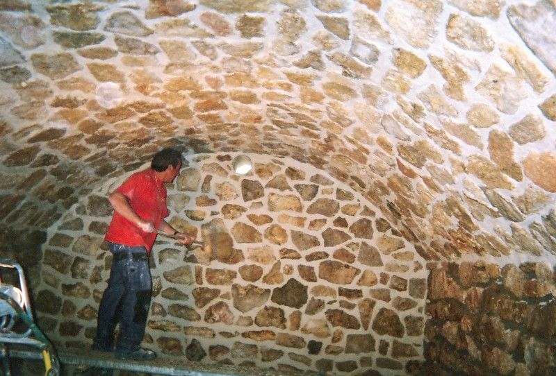 Une personne en chemise rouge travaille à l'intérieur d'une salle voûtée aux murs de pierre