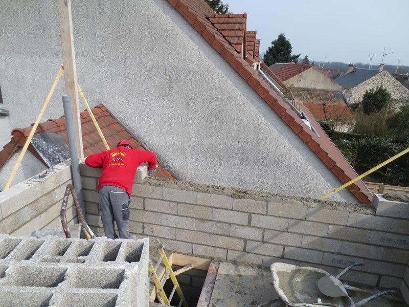 Un ouvrier en chemise rouge se trouve sur un toit, s'appuyant contre un mur incliné pendant les travaux de construction.