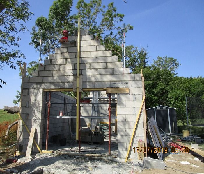 Maison en parpaings partiellement construite, avec une porte ouverte et des ouvriers sur le toit sous un ciel bleu