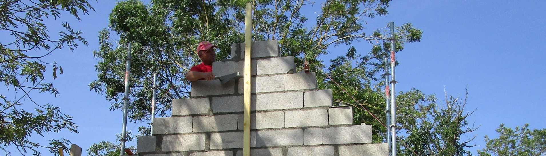 Une personne vêtue d'une chemise rouge se tient au sommet d'une pyramide en béton, à l'extérieur, au milieu des arbres.