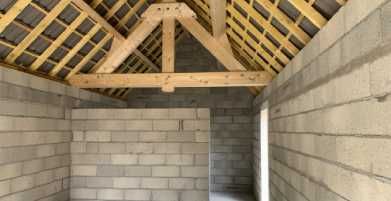 Pièce inachevée en construction, avec murs en parpaings et charpente apparente en bois.