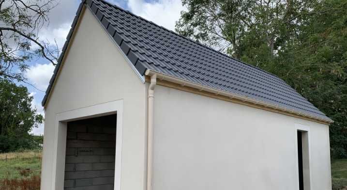 Petite maison blanche avec un toit à pignon gris foncé et une porte ouverte de type garage.