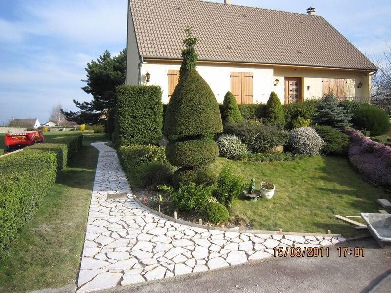 Une maison avec un jardin soigné, des haies taillées et une allée en pierre par une journée ensoleillée