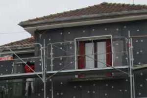 Extérieur de la maison avec échafaudages en construction, façade grise et toit en tuiles rouges