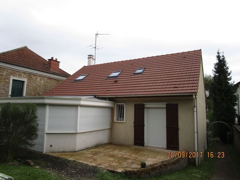 Petite maison avec toit de tuiles rouges, volets blancs et patio dans une cour résidentielle