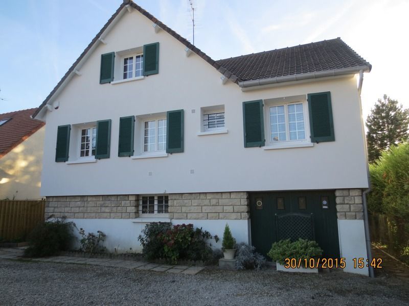 Maison blanche à deux étages avec volets verts, garage et allée de gravier.