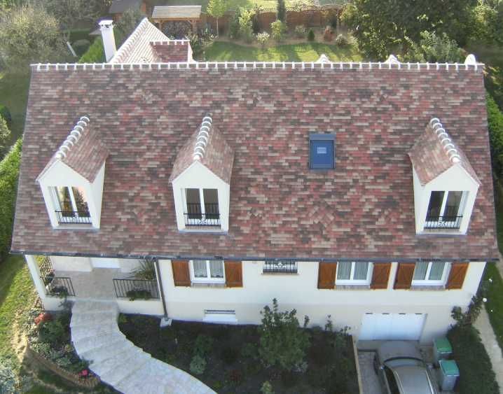 Vue aérienne d'une maison avec un toit de tuiles rouges, des murs blancs, des lucarnes et une allée courbe.