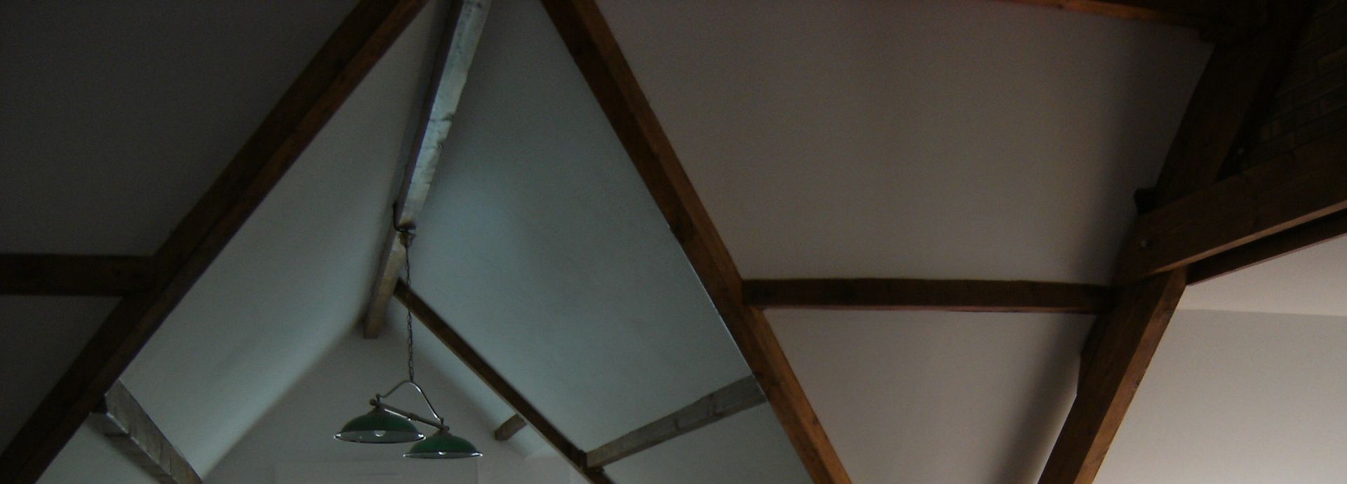 Poutres apparentes en bois avec un luminaire suspendu et un ventilateur de plafond sur un plafond voûté blanc.