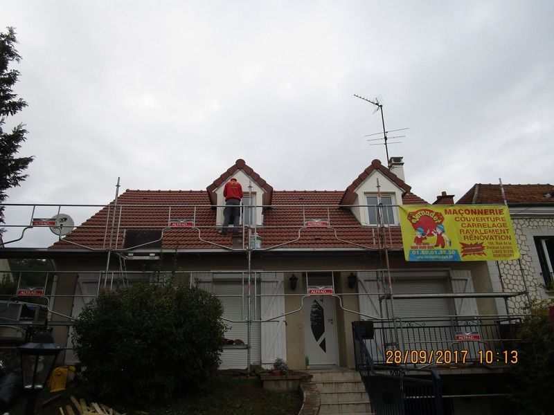 Maison à deux étages avec un toit de tuiles rouges, des murs blancs et une enseigne jaune sous un ciel nuageux.